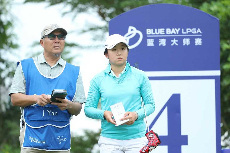 大赛背景下，父亲作为球童坚定地站在女儿身后，满怀信任地注视着她准备关键一击。