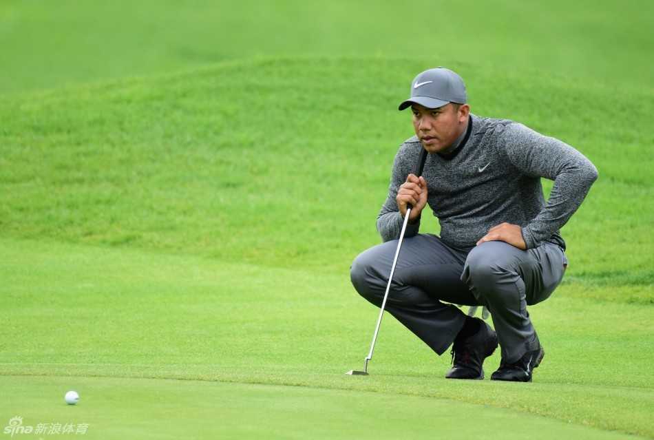 一辆赛事球车载着球员和球包在空旷潮湿的球道上行驶，驶离被风雨笼罩的比赛现场，画面充满故事感。