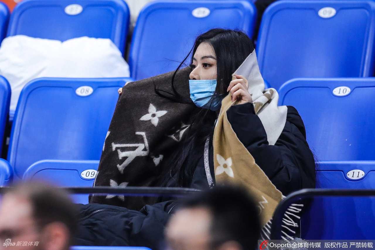 杨诗尹面带微笑注视着球场方向，即使戴着口罩也难掩其清秀眉眼。在体育馆背景的映衬下，她那份由内而外散发的自信与淡定，成为看台上一道独特的风景线。