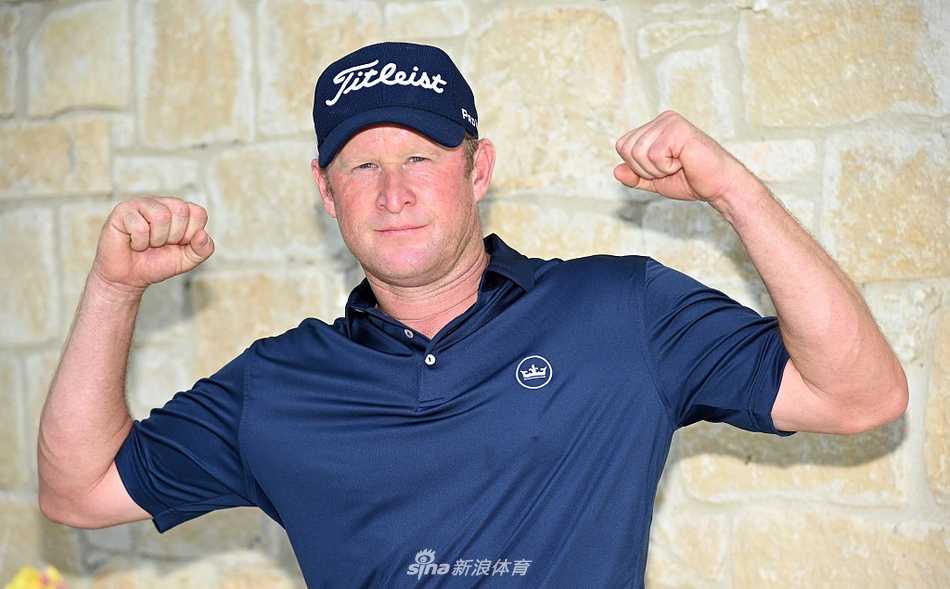 马来西亚球手加文·格林在果岭边细致观察推杆线路，起伏的果岭与远方的度假村建筑构成宁静画面。