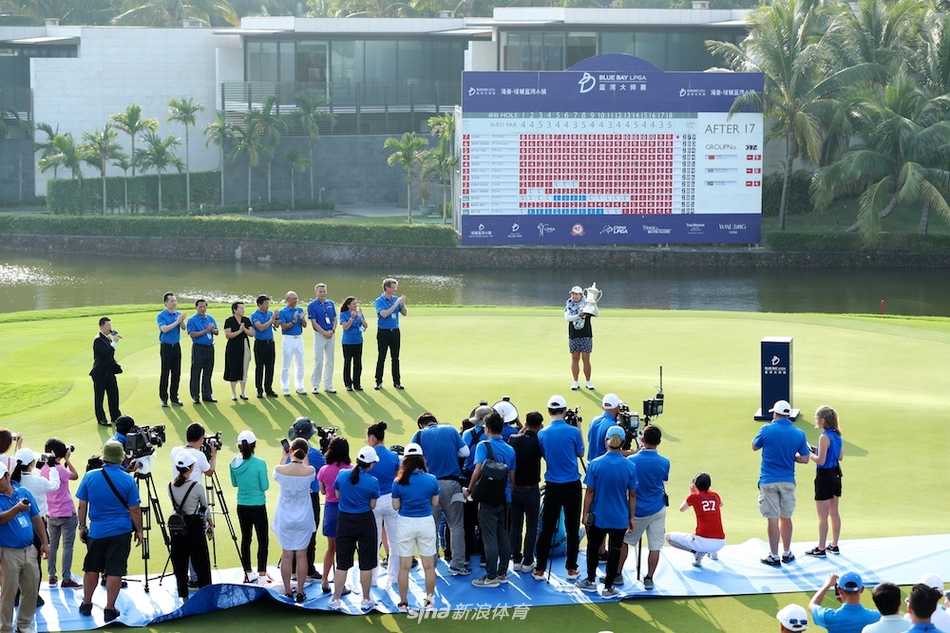 冯珊珊在果岭上高举冠军奖杯，向全场观众展示这一荣耀时刻，背景是蓝湾大师赛的标志与热烈鼓掌的人群。