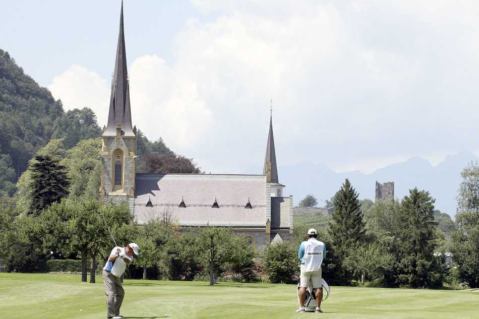 阳光洒在修剪完美的球道果岭上，球员们正在认真推杆，背景中经典的俱乐部会所与群山相映成趣。