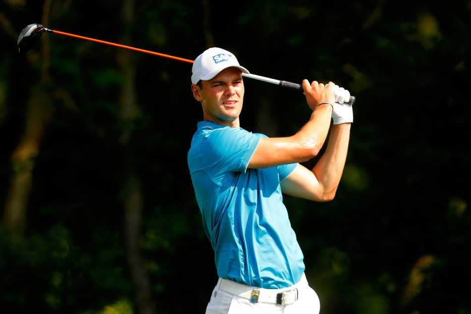 丹麦高尔夫球星托马斯-比约恩站在沙坑边缘，双手叉腰，蹙眉审视着坑中的小球，正在构思脱困的最佳击球策略。