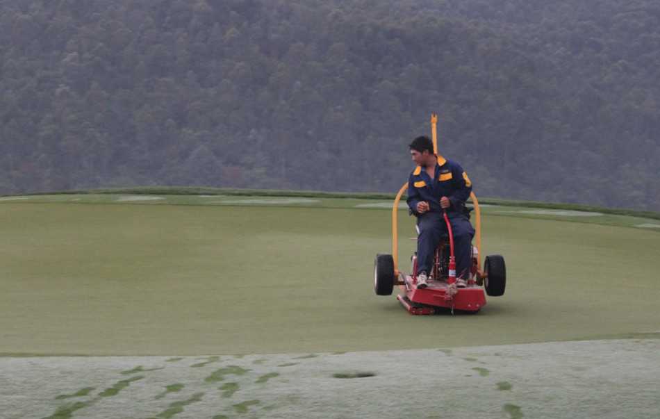 破晓时分的高尔夫球场养护交响曲 养护人员手持果岭测速仪,弯腰凝视着白色小球在翠绿的果岭表面滚动的轨迹,全神贯注地记录下决定今日比赛难度的关键数字。