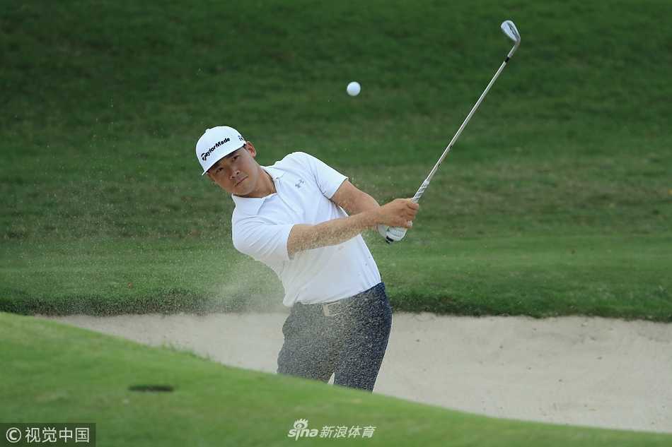 中国高尔夫球手张新军专注地进行沙坑救球练习，白沙与果岭的翠绿形成鲜明对比，展现了其细腻的短杆技术。