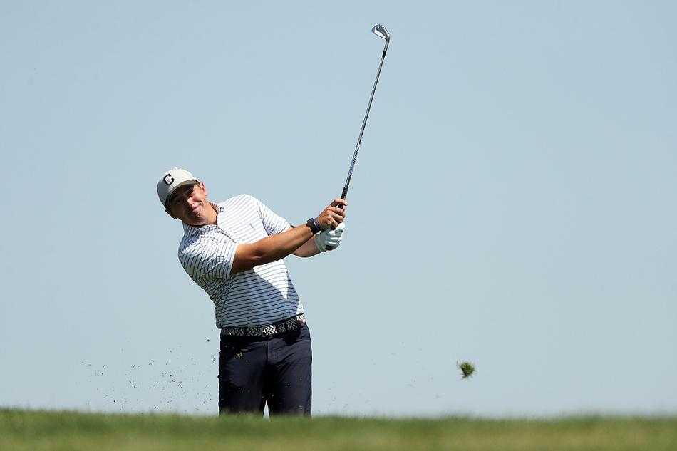 球员使用挖起杆从果岭旁沙坑中击球，沙粒随之飞扬形成一道金色烟雾