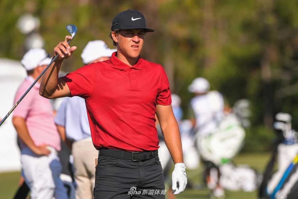 一位球员的背影行走在开阔的球道上，鲜红的衣衫在广阔的绿地与天空之间成为一抹亮色，象征着希望与陪伴在征途上延续。