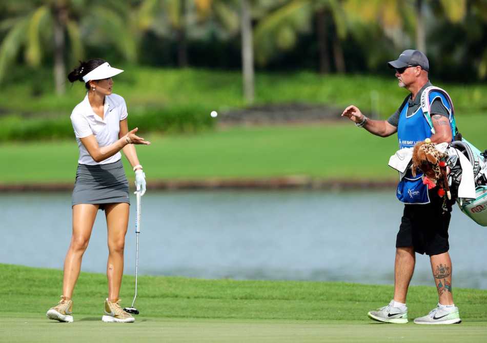 魏圣美在果岭旁微笑着将高尔夫球轻抛给球童，画面充满了搭档间的信任与比赛的轻松一刻。