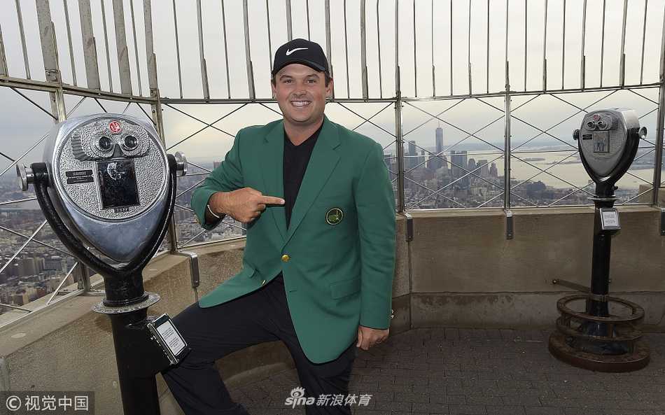 绿夹克闪耀纽约之巅 新科大师赛冠军瑞德的荣耀巡礼 帕特里克·瑞德身着大师赛冠军绿夹克,在帝国大厦观景台手持签名果岭旗,背后是朦胧的纽约城景
