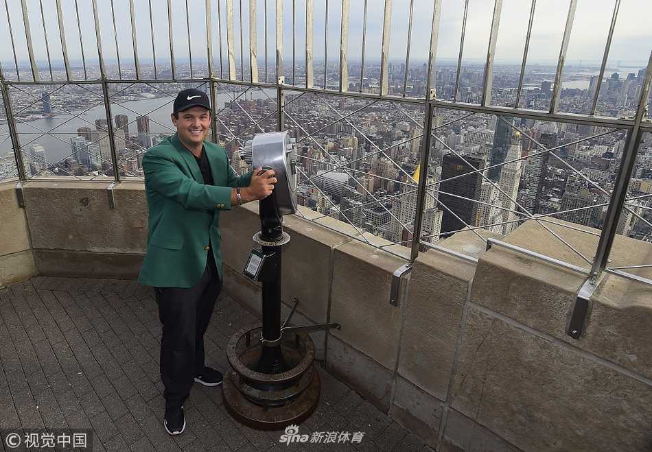 绿夹克闪耀纽约之巅 新科大师赛冠军瑞德的荣耀巡礼 瑞德与妻子在帝国大厦观景台亲密相拥,两人笑容幸福,身后的绿夹克是他们共享胜利喜悦的见证