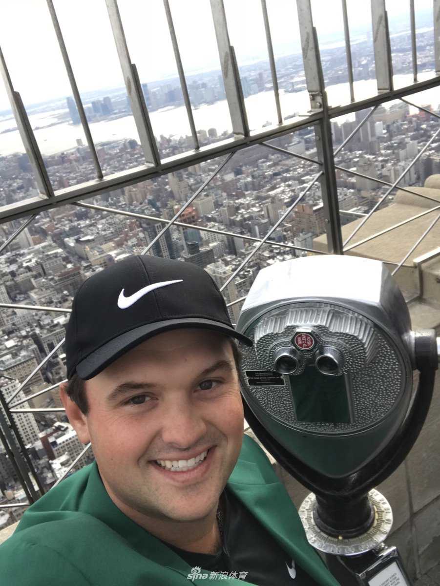绿夹克闪耀纽约之巅 新科大师赛冠军瑞德的荣耀巡礼 冠军瑞德在观景台上举起手机自拍,脸上洋溢着灿烂笑容,绿夹克在阳光下格外醒目