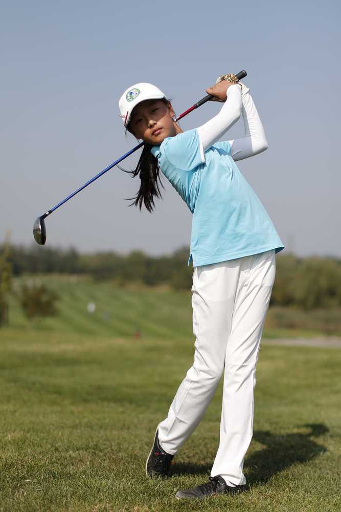 练习场上，一位小球员正专注于调整自己的挥杆姿势，眼神坚定，身影在草地上拉得修长。