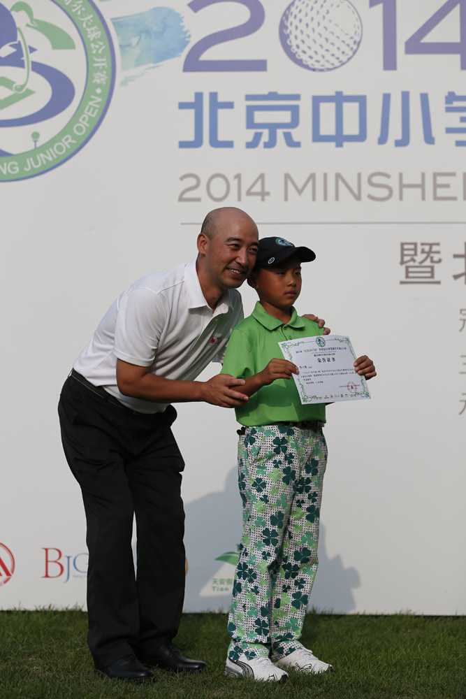 一位幸运的小球员荣获‘一杆进洞奖’，他高举奖杯，脸上写满了惊喜与自豪，身边的伙伴们也为他欢呼。