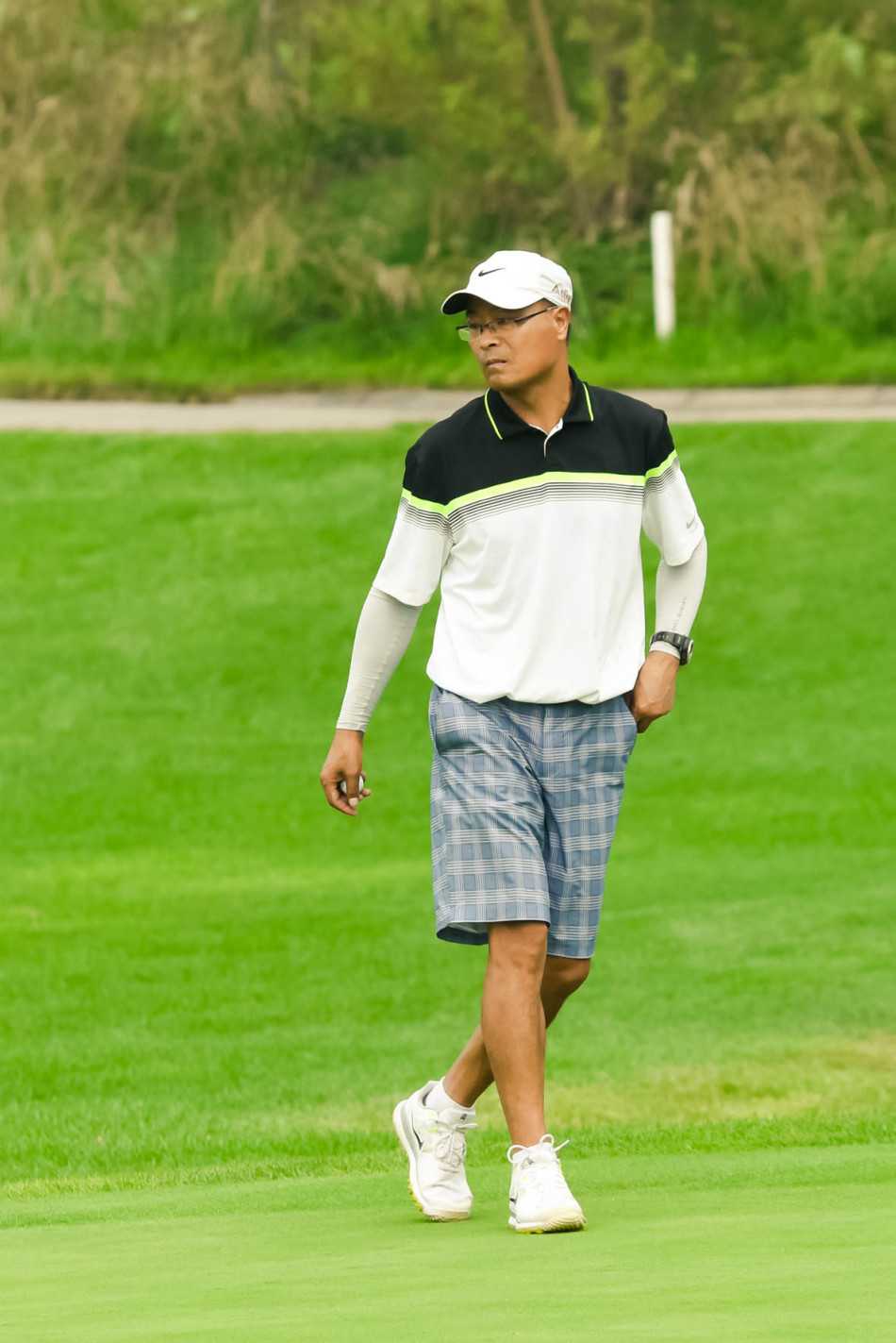 绿茵之上的优雅对决 球员在果岭上轻轻标记起自己的小球,背景是广阔的球场与蓝天,展现了高尔夫运动特有的宁静与专注