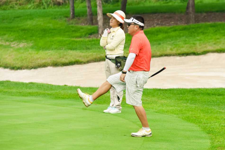 绿茵之上的优雅对决 身着红色球衣的球员迈克,正站在果岭上沉稳地准备推杆,阳光洒在他和绿色的果岭上,静谧而充满张力