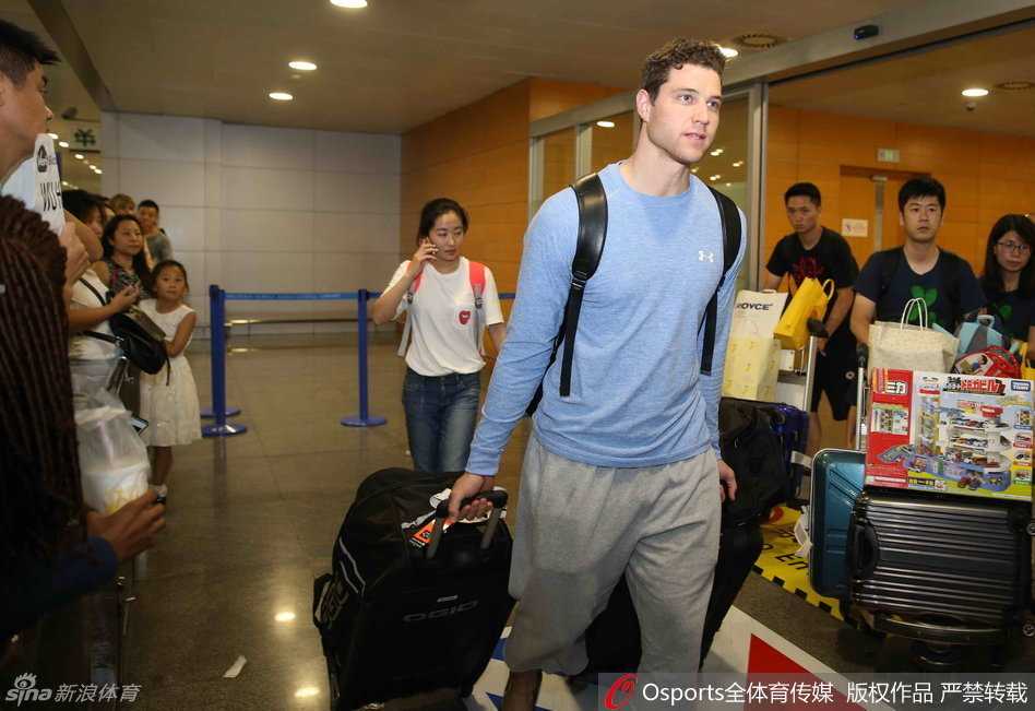 站在机场扶梯上的弗雷戴特，低头凝视着下方的接机人群，嘴角浮现出一丝略带羞涩却又温暖的微笑，仿佛在与这座即将托付未来的城市进行第一次无声的对话。