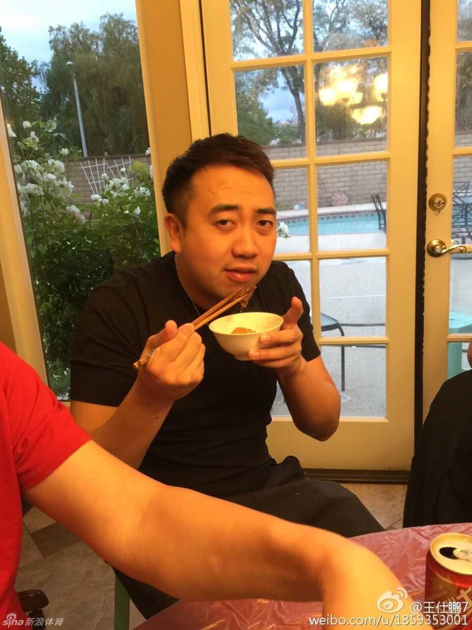 聚会尾声众人起身离席，易建联披着外套与王仕鹏勾肩搭背，刘宏疆在旁微笑，窗外夜色中洛杉矶灯火闪烁