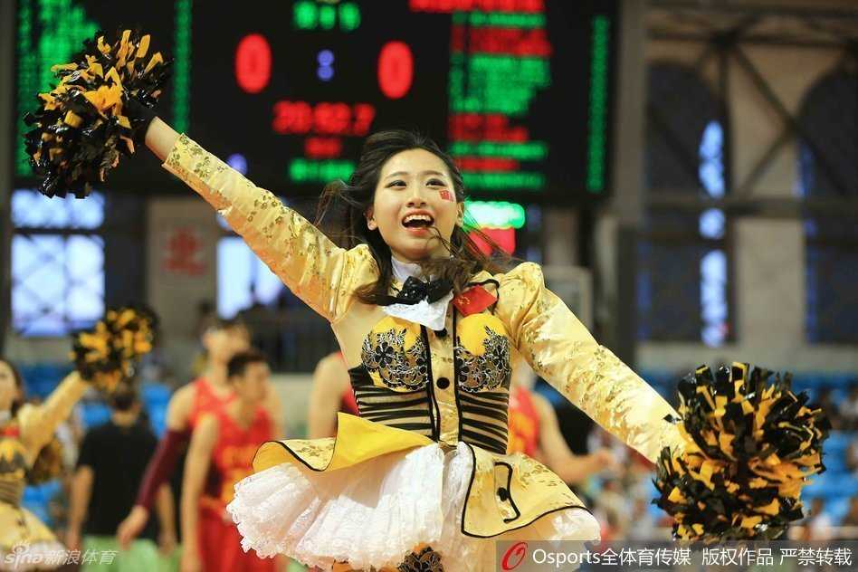 在场地中央，一名篮球宝贝正完成一个高难度的下腰动作，她身体向后弯曲成一道优美的弧线，长长的秀发几乎垂到地面，周围队友们则围成一个圈为她鼓掌喝彩，展现出团队之间的默契与信任。