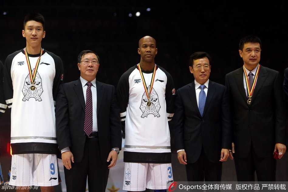 比赛暂停间隙，北京队主教练闵鹿蕾手持战术板，神情严肃地为队员们布置战术，他的身后是刚刚升起的总冠军旗帜，此刻球队正面临严峻考验。