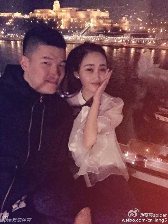 休闲时光的甜蜜定格:篮球明星蔡亮与未婚妻的幸福求婚记 两人在一个充满设计感的卡通雕塑旁合影,蔡亮搞怪地模仿着雕塑的动作,逗得身边的未婚妻开怀大笑,画面充满了青春的活力与俏皮。