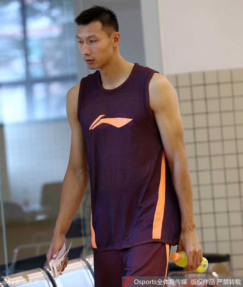 岭南剑客蓄力中:粤媒镜头下的宏远众生素描 健身房的全景图,董瀚麟与多名年轻队员正在体能教练的指导下进行牵拉放松,气氛严肃而专注,墙上的宏远队徽在灯光下熠熠生辉,见证着每一份努力。