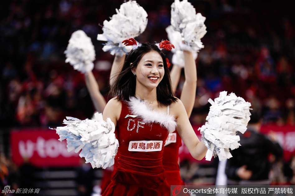 拉拉队圣诞热力秀,点燃萧瑟冬日球场 一位队员的特写,她手持啦啦球花,背景是模糊的看台观众,红色的圣诞装和专注的神情完美诠释了球场上的节日氛围。