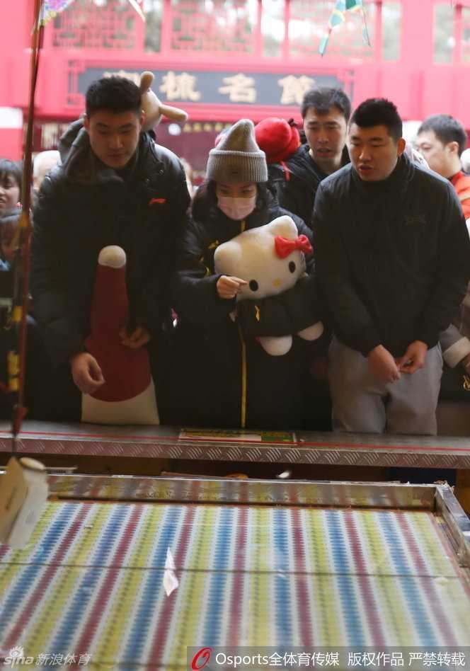 春节邂逅温情:篮球国手常林地坛庙会秀最萌身高差 逛累了的常林与女伴在庙会休息区小憩,他手中依然抱着那个大玩偶,脸上带着些许疲惫却十分满足的神情,身后是庙会熙熙攘攘的人流和喜庆的装饰。