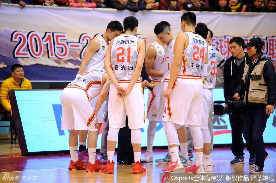 残阵铁军憾负青岛,八一禁赛阴霾下显军魂 首发队员准备上场,五名先发球员神色凛然地站在中圈附近,他们身后巨大的八一军旗图案仿佛在燃烧,映照着勇士们无畏的脸庞。