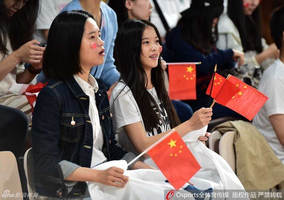 法兰西之夏:那一抹飘扬的中国红与女篮的里约之梦 镜头聚焦于一位正在整理妆容的中国美女球迷,她修长的手指轻轻撩起乌黑的长发,眼神专注而温柔,随后将一枚五星红旗贴纸端正地贴在脸颊上,青春洋溢的脸上写满了对女篮的期盼与祝福。