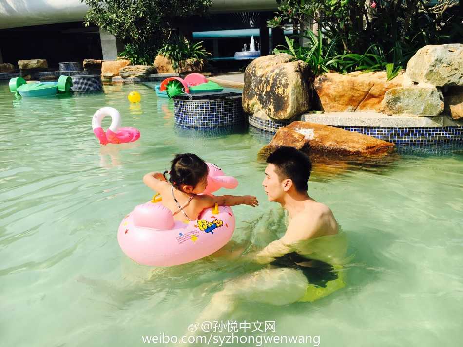 孙悦搞怪地将头探入女儿的小游泳圈中，假装成顽皮劫匪，手持水枪准备喷射