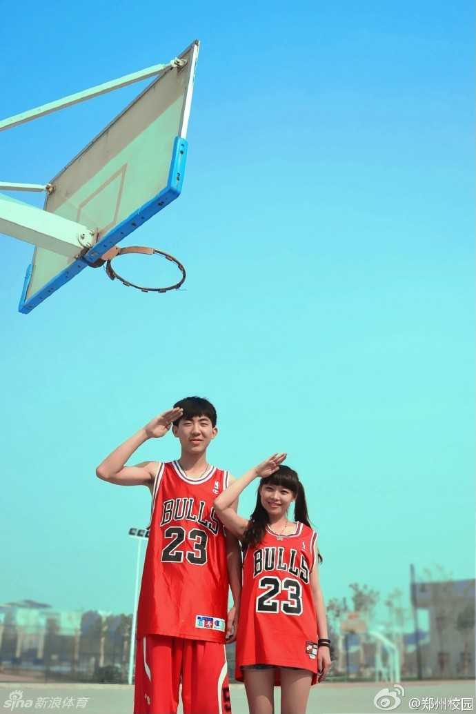 在校园篮球场上，身穿深色球衣的少年高高跃起，全力以赴地给对方一个结实的封盖，而场边观众的目光都聚焦在这场激烈的对抗上，充满了竞技的张力。