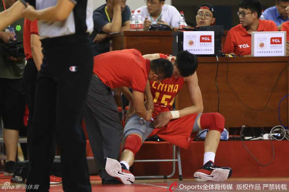 男篮热身赛惊魂一刻:周琦意外受伤痛苦倒地,队友揪心队医紧急治疗 队医单膝跪地,神情专注而紧张,手中拿着喷雾剂为周琦的伤处紧急降温镇痛。周琦依旧趴在地上,只能微微抬起头,眼神中透露出难以掩饰的痛苦与不甘。