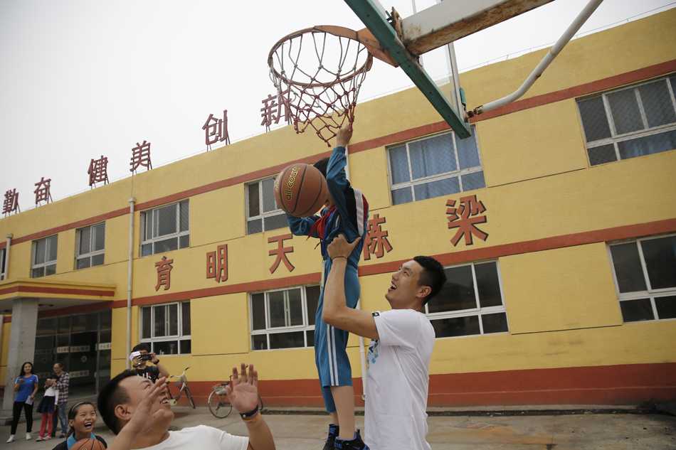翟晓川赴昌平春风学校献爱心 为打工子弟点亮希望之光 翟晓川与全校师生的大合影中,孩子们举着崭新的文体用品欢呼雀跃,背景是略显斑驳的教学楼,但每个人的笑容都如同阳光般灿烂