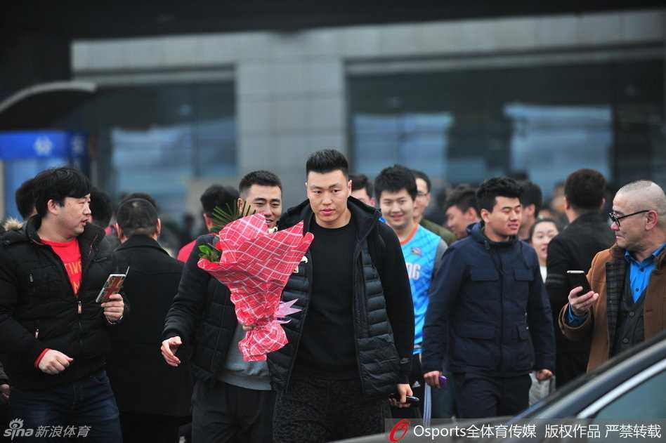 一位身穿新疆队球衣的女球迷低着头，专注地在手中的本子上寻找空白位置，准备请经过的球员签名。