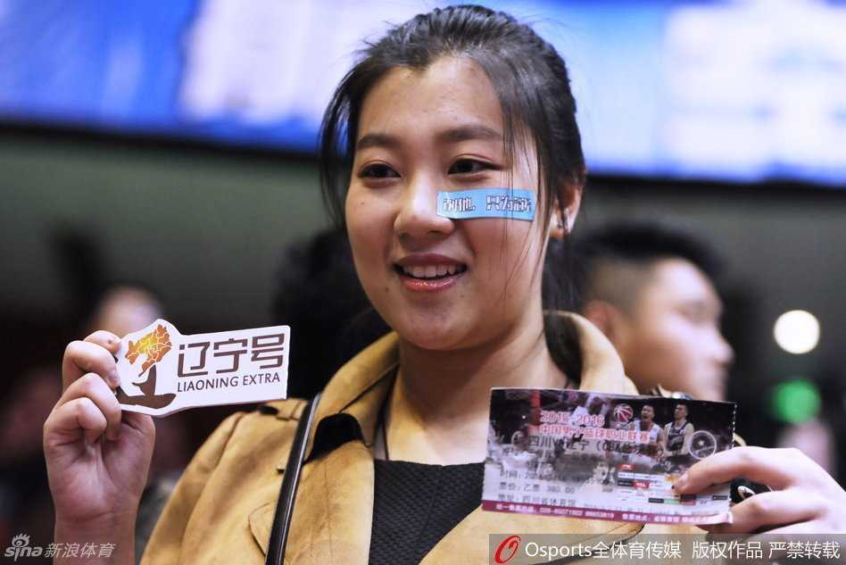 一位容貌清秀的女球迷，脸上画着红色的心形图案，在人群中安静地注视着赛场，眼神中透露出对比赛的专注和对偶像的支持，仿佛整个世界只剩下了她与那片球场。