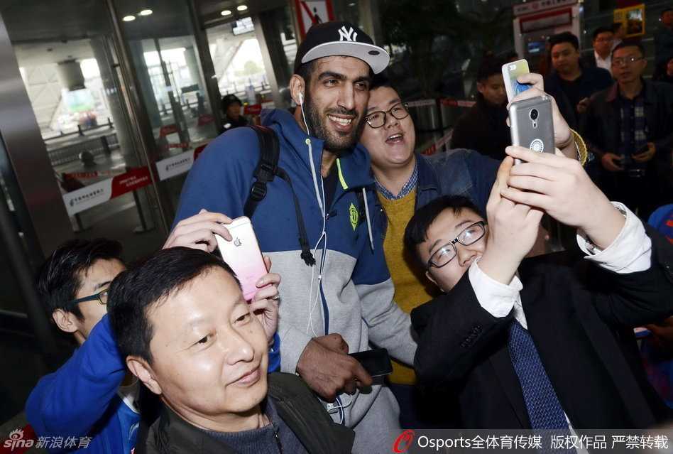 身披四川队战袍的功勋外援哈里斯，在机场被热情的球迷团团围住，他面带标志性的灿烂笑容，正俯身与一位小球迷击掌互动。