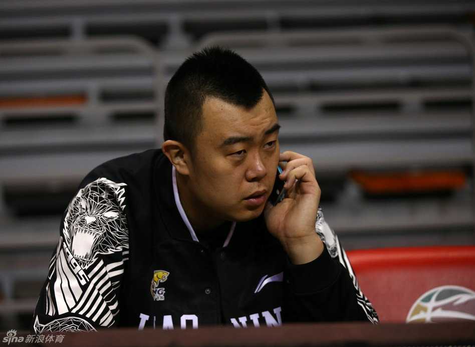 主教练郭士强在场边接受媒体采访，表情认真严肃，拿着战术板的手势显示出他对球队战术细节的严格把控
