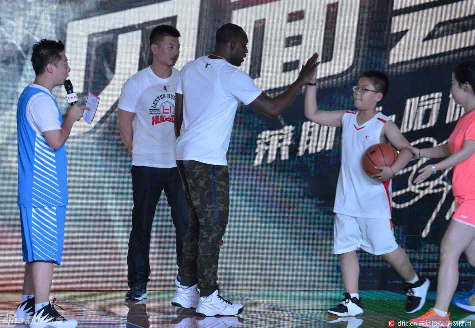 哈德森怀抱着粉丝送上的鲜花，身旁站着可爱的女儿，父女俩一起对着镜头露出幸福的笑容，背景是热情的沈阳球迷。