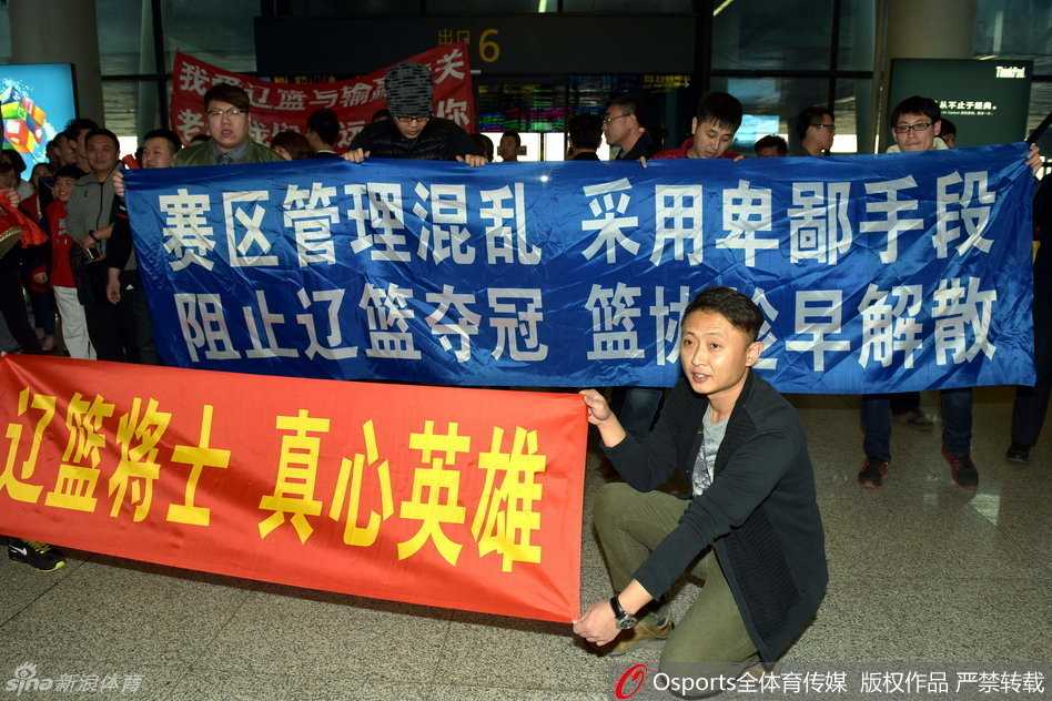 辽沈球迷含冤接机,标语声声讨伐篮协不作为 在拥挤的人群中,辽宁男篮主教练郭士强被特警和安保人员紧紧护在中间,他面色凝重,望着不远处那些举着支持标语却无法靠近的球迷们。
