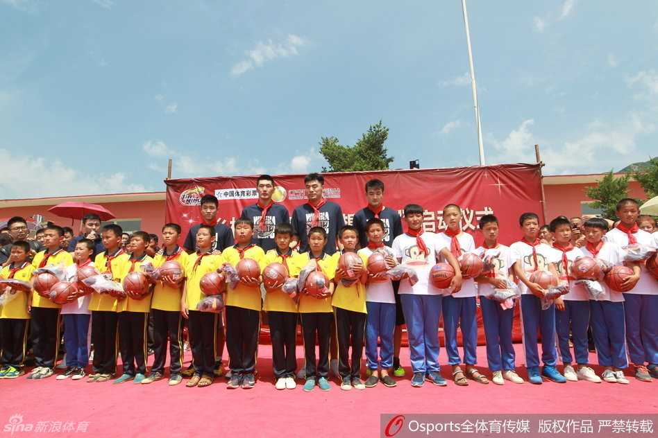 辽篮主帅郭士强手持话筒，正在讲话，身后的孩子们和辽篮队员们认真聆听，每个人的脸上都洋溢着对篮球的热爱。