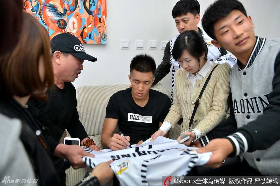 郭艾伦坐在休息区的椅子上，耐心地给一位小球迷递过来的球衣签名，他低垂着眼帘，神情专注，小球迷则在一旁紧张又期待地看着。