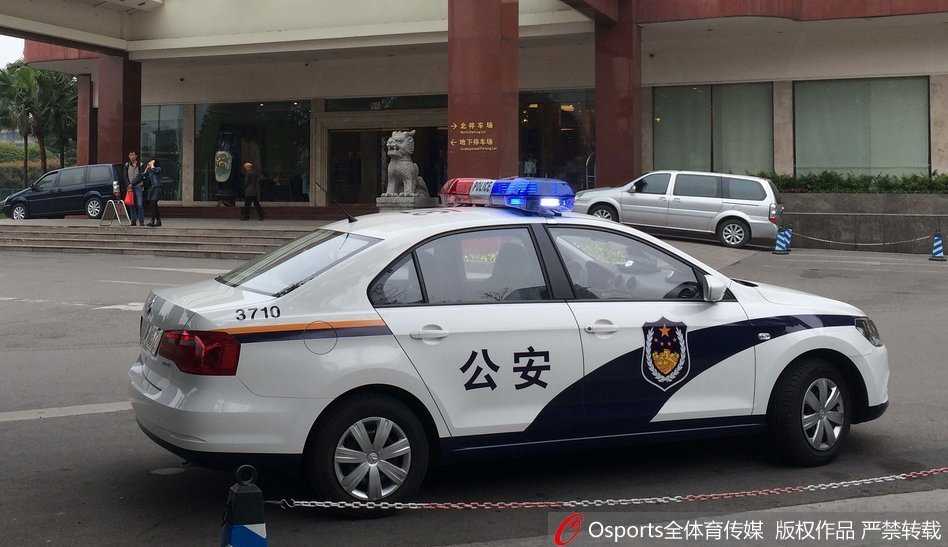 成都锦江宾馆正门口气氛凝重，一辆警车闪烁着警灯静静驻守，蓝白相间的车身与酒店大理石外墙形成冷峻对比，仿佛在无声宣告着特殊时期的安全警戒。