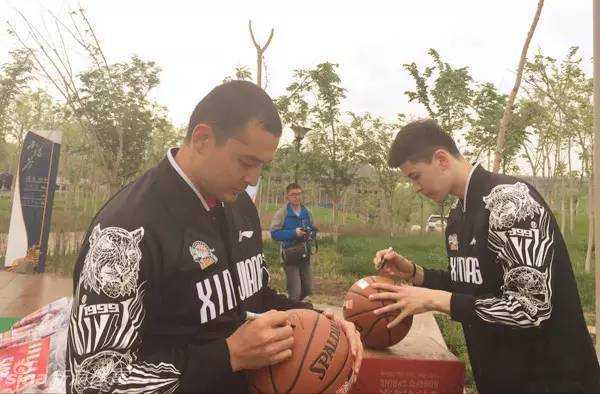 风雨同行,为爱酷跑:西热力江与阿不都的公益征途 西热力江俯身给手中的篮球签名,他签得非常投入和细致,希望通过这颗篮球传递更多的爱心与正能量。
