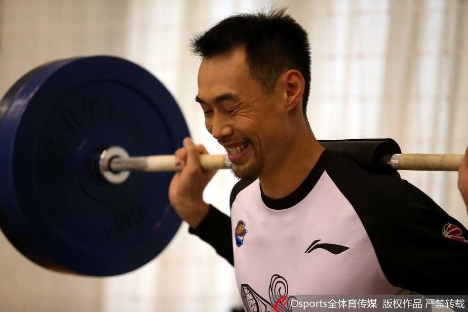 一名球员正在进行负重深蹲的预备动作，他双手紧握杠铃杆，眼神坚定地盯着前方，准备迎接这组极限挑战。