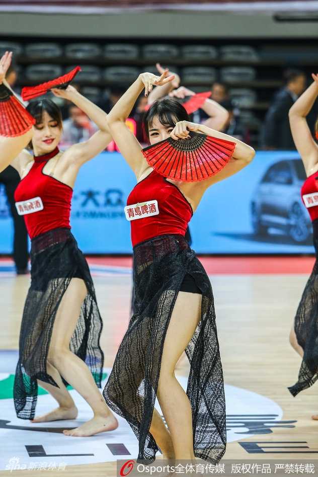 广厦队与浙江队在场上激烈拼抢的瞬间被定格，而在背景处，刚刚完成表演的蕞红啦啦队正在退场。她们红色的裙摆在人群中格外显眼，仿佛战火纷飞的古战场边那一抹温柔的霞光，一动一静之间，诠释了竞技体育的刚与艺术表演的柔。