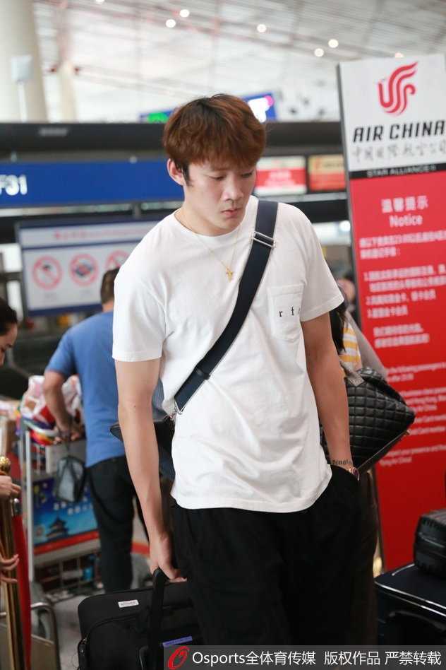 丁彦雨航在酒店大堂接受媒体采访，虽然面带旅途的倦容，但谈及归队心情时，他眼神坚定，嘴角带着笑意，身后的背景是酒店内来往的人群。