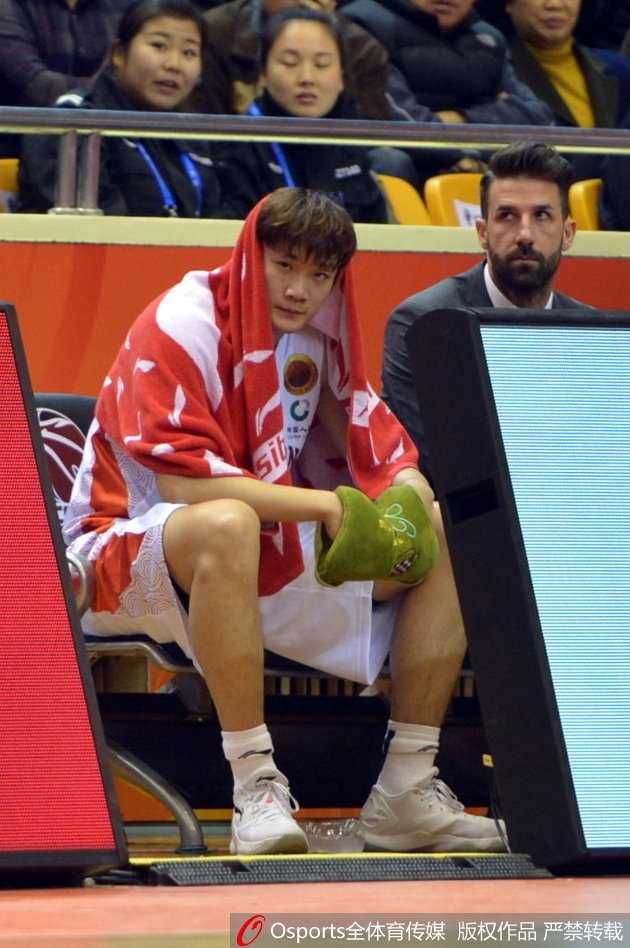 小丁抱着篮球在更衣室，歪着头看着镜头，脸上挂着腼腆而温暖的笑容。