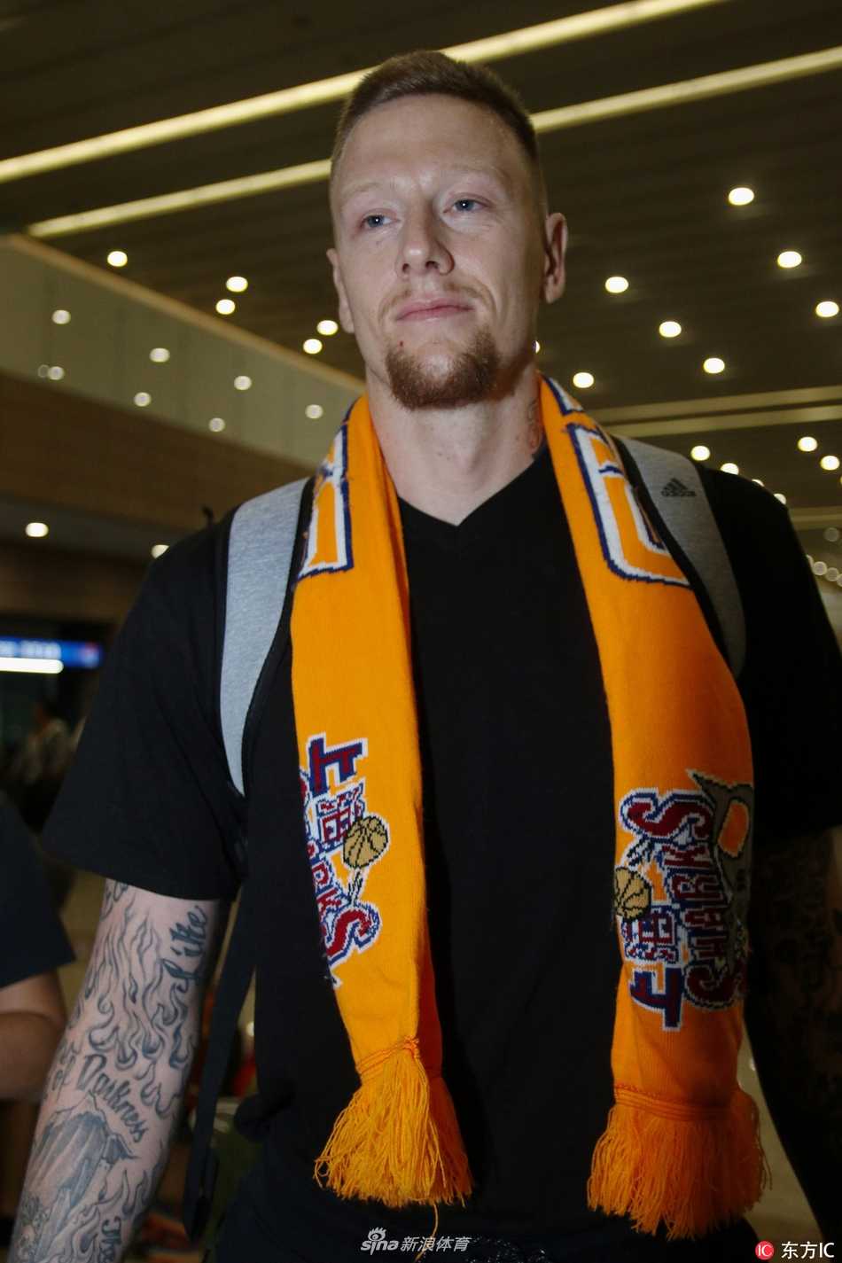 身形高大的明纳拉斯身着一袭休闲黑衣，与金发妻子并肩走出通道，脸上洋溢着初来乍到的灿烂笑容，仿佛对这座城市和新赛季充满无限憧憬