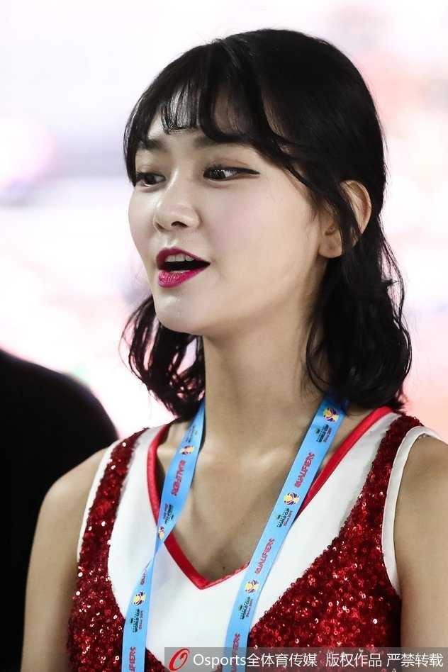 礼仪小姐在灯光下微微低头，光影勾勒出柔和的轮廓，手中标牌与古典发髻构成一幅静谧美好的画面