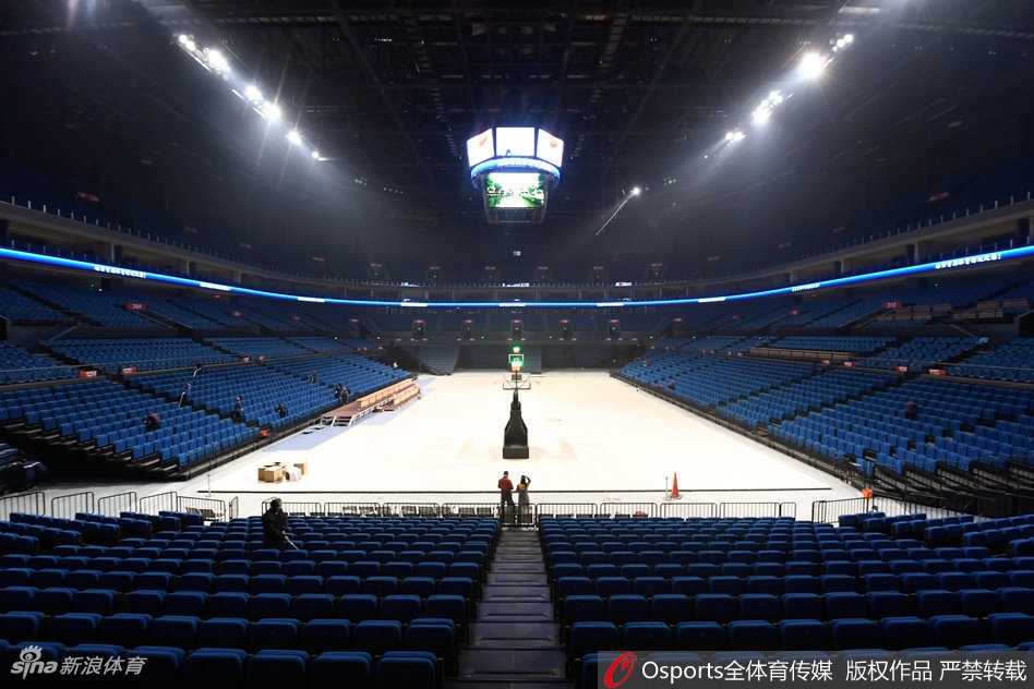 从高空俯瞰体育馆内部，巨大的中央漏斗屏正闪烁着红色的中国地图，四周看台上身着红色助威T恤的球迷座无虚席，汇成一片红色的海洋，场中央的球员正在灯光的聚焦下进行赛前热身。